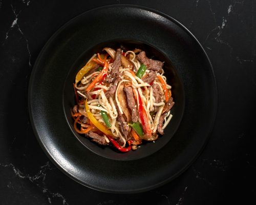 Traditional Asian Pasta. udon noodles with beef and vegetables on a plate on black stone background. Flat lay, Wok menu. Top view